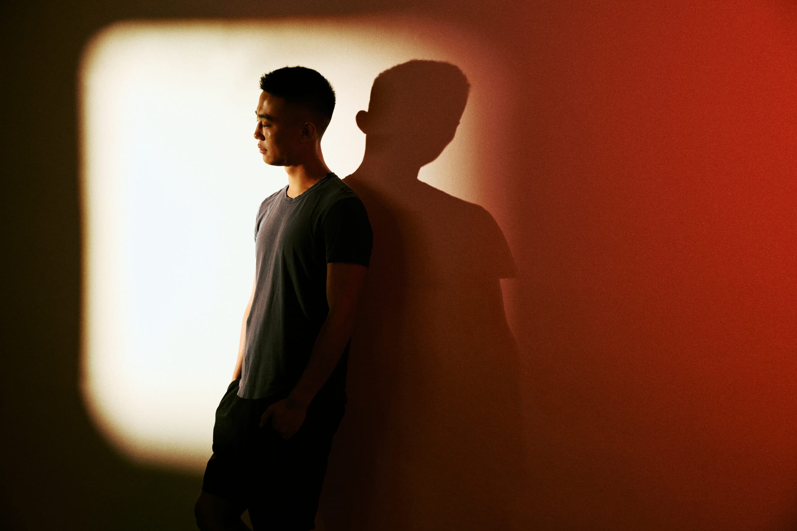 Jeff Yan leaning against a wall in a T-shirt and shorts.